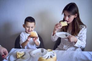 familie van drie, moeder, tiener- dochter en weinig zoon, aan het eten taart in pyjama Bij een tafel met tulpen foto