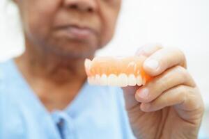 Aziatisch senior vrouw geduldig schoon tanden kunstgebit met tandenborstel voor kauwen voedsel. foto
