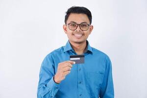 glimlach of gelukkig jong Aziatisch zakenman met bril Holding credit kaart vervelend blauw overhemd geïsoleerd Aan wit achtergrond foto