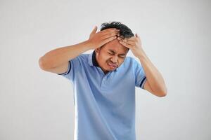 Aziatisch Mens hoofd in pijn, Holding hoofd met beide handen vervelend blauw t overhemd geïsoleerd Aan wit achtergrond foto