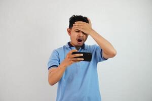 jong Aziatisch Mens de effect van wezen teleurgesteld wanneer u verliezen spelen een spel online met smartphone en Holding uw voorhoofd geïsoleerd Aan wit achtergrond foto