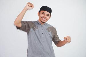 zelfverzekerd vrolijk knap Aziatisch moslim Mens hijs- handen omhoog vervelend koko kleren voelt geluk tonen vuist omhoog succes geïsoleerd Aan wit achtergrond foto