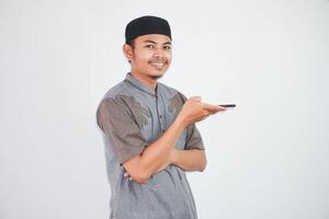 jong Aziatisch moslim Mens glimlach pratend gebruik makend van de stem assistent Aan mobiel telefoon vervelend moslim kleren geïsoleerd Aan wit achtergrond foto