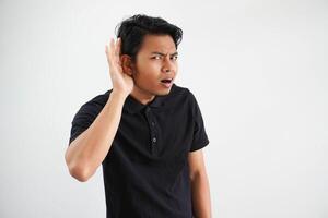 jong Aziatisch Mens op zoek camera en aan het doen kan niet horen gebaar, proberen naar luisteren een roddel vervelend zwart polo t overhemd geïsoleerd Aan wit achtergrond foto