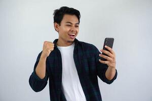 jong Aziatisch Mens balanceren vuist tonen opwinding wanneer op zoek naar zijn telefoon geïsoleerd Aan wit achtergrond foto