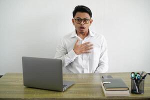 jong Aziatisch zakenman in een werkplaats verrast en geschokt terwijl op zoek vooruit met handen aanraken borst slijtage wit overhemd geïsoleerd foto