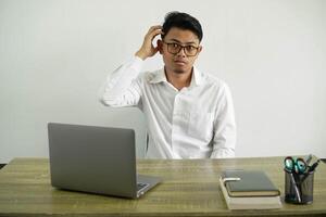 jong Aziatisch zakenman in een werkplaats met een uitdrukking van frustratie en niet begrip, vervelend wit overhemd met bril geïsoleerd foto