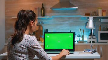 bedrijf vrouw op zoek Bij groen scherm laptop zittend Bij huis in keuken. freelancer aan het kijken bureaublad toezicht houden op Scherm met groen model, chroma sleutel, gedurende nacht tijd werken na een tijdje. foto