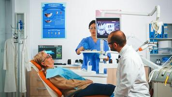 Mens tandheelkunde dokter richten Aan digitaal scherm tonen tandheelkundig implantaten. tandarts en verpleegster werken samen in modern stomatologisch kliniek, uitleggen radiografie van tanden Aan toezicht houden op foto
