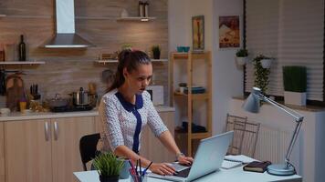 zakenvrouw typen Aan laptop terwijl werken van een afstand laat in huis keuken. bezig gefocust werknemer gebruik makend van modern technologie netwerk draadloze aan het doen na een tijdje voor baan lezing schrijven, zoeken foto