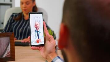 gehandicapt zakenman pratend Aan video telefoontje met dokter in werk tijd zittend in rolstoel in modern bedrijf kantoor gebruik makend van smartphone. van een afstand medisch adviseren freelancer gebruik makend van modern technologie foto