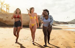 gelukkig multiraciaal vrouwtjes met verschillend lichaam grootte hebben pret wandelen Aan de strand gedurende zomer vakantie foto
