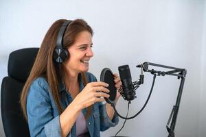 volwassen vrouw opname een podcast gebruik makend van microfoon en hoofdtelefoons van haar huis studio foto