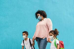 moeder met zoon en dochter terug naar school- terwijl vervelend gezicht beschermend masker gedurende corona virus pandemisch - gezondheidszorg en onderwijs concept foto