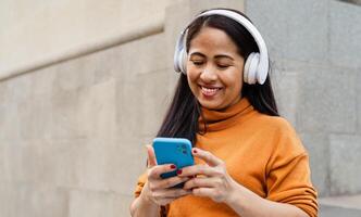 gelukkig zuidoosten Aziatisch vrouw luisteren naar muziek- met mobiel smartphone en hoofdtelefoons in de stad centrum foto