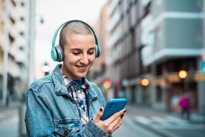 geschoren hoofd meisje gebruik makend van mobiel smartphone en luisteren muziek- terwijl aan het wachten voor openbaar vervoer in de stad straat foto