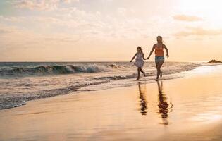 gelukkig liefhebbend familie moeder en dochter rennen Aan de strand Bij zonsondergang - mamma hebben pret met haar kind lang zee kust gedurende zomer vakantie - ouder vakantie tijd levensstijl concept foto