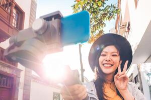 Aziatisch vrouw maken video blog met smartphone gimbal buitenshuis - gelukkig Aziatisch influencer hebben pret met nieuw technologie trends voor sociaal media - mensen, generatie z, tech en jeugd levensstijl concept foto