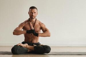 een Mens met een naakt torso is zittend in de lotus positie voordat aan het doen yoga binnenshuis. geschiktheid trainer foto