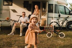 een jong familie is resting De volgende naar hun mobiel thuis.a meisje Toneelstukken bambinton in de buurt een mobiel huis foto