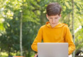 attent tiener jongen werken Aan laptop. Holding en gebruik makend van een laptop voor netwerken Aan een zonnig voorjaar dag, buitenshuis. foto