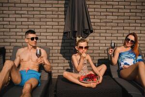 een gelukkig familie in zwemkleding zonnebaden in zomer Aan hun terras Aan zon bedden foto