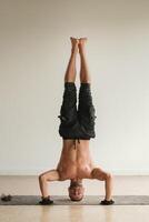 een Mens met een naakt torso doet yoga staand Aan zijn hoofd binnenshuis. geschiktheid trainer foto