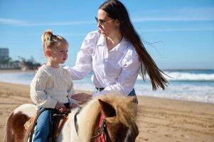 Kaukasisch jong vrouw, een liefhebbend zorgzaam moeder onderwijs haar lief kind naar stijgen een paard pony. mensen. natuur. dieren. foto