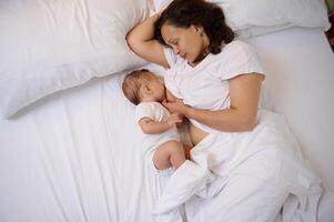 top visie schattig baby jongen 4 maanden oud zogen de melk van moeder borst, aan het liegen samen Aan de comfortabel bed Bij huis foto