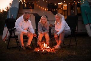 een familie kookt worstjes Aan een vreugdevuur in de buurt hun camper in de bossen foto