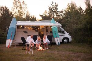 een familie kookt worstjes Aan een vreugdevuur in de buurt hun camper in de bossen foto