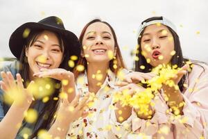 gelukkig Aziatisch vrienden hebben pret het werpen confetti buitenshuis - jong modieus mensen vieren carnaval festival zelfs - partij vermaak en jeugd vakantie levensstijl concept foto