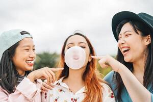 gelukkig Aziatisch vrienden hebben pret kauwen bubbel gom buitenshuis - jong mensen spelen en lachend samen - vriendschap, millennial generatie en jeugd levensstijl concept foto