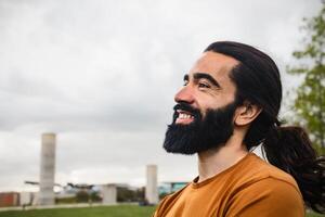 gelukkig gebaard Mens met lang haar- hebben pret glimlachen in een park foto