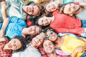 groep van verschillend vrienden hebben pret buitenshuis - gelukkig jong mensen aan het liegen Aan gras na picknick en lachend samen - vriendschap, eenheid, millennial en jeugd levensstijl concept foto