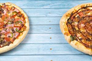 twee verschillend heerlijk groot pizza's Aan een blauw houten achtergrond foto