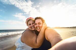 gelukkig plus grootte Dames nemen selfie Aan de strand - golvend te zwaar meisjes hebben pret gedurende vakantie in tropisch bestemming - over- grootte zelfverzekerd mensen levensstijl concept foto