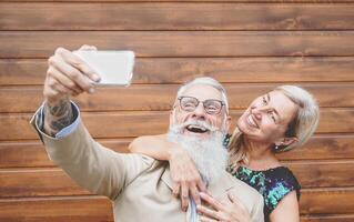 senioren paar lachend en nemen selfie met mobiel smartphone camera - sociaal volwassen mensen hebben pret met nieuw modieus technologie - tech en ouderen levensstijl werkzaamheid foto