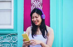 gelukkig Aziatisch meisje luisteren naar muziek- met hoofdtelefoons buitenshuis - jong Chinese vrouw spelen haar favoriete afspeellijst muziek- van haar mobiel smartphone app - millennial generatie en technologie concept foto