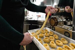 dichtbij omhoog mannetje handen voorbereidingen treffen vers fettucine gebruik makend van machine binnen pasta fabriek foto