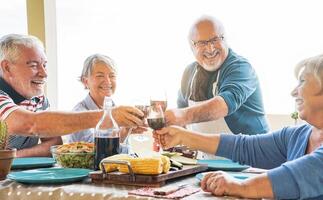 gelukkig senior vrienden roosteren met rood wijn Bij barbecue avondeten in terras - volwassen mensen dining en juichen samen drinken wijn Aan op het dak - vriendschap, voedsel en ouderen levensstijl concept foto