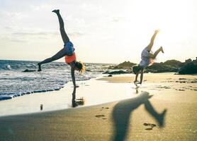 gelukkig liefhebbend familie van Mather en dochter hebben pret maken acrobatisch handstand Aan de strand Bij zonsondergang - jong mam genieten van tijd met haar kind spelen samen oudoor - familie levensstijl concept foto