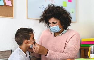 leraar vrouw zetten gezicht beschermend masker naar leerling in peuter- klas gedurende corona virus pandemisch - gezondheidszorg en onderwijs concept foto