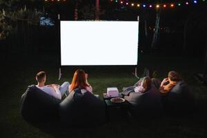 familie moeder, vader en kinderen kijk maar een projector, films met popcorn in de avond in de binnenplaats foto