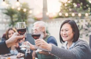 gelukkig familie aan het eten en drinken rood wijn Bij avondeten barbecue partij buitenshuis - volwassen en jong mensen dining samen Aan terras - jeugd en ouderen weekends levensstijl activiteiten en voedsel concept foto