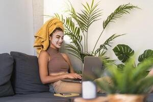 jong vrouw gebruik makend van laptop terwijl hebben huid zorg dag Bij huis foto
