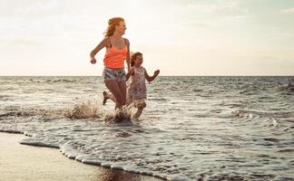 gelukkig liefhebbend familie moeder en dochter rennen Aan de strand Bij zonsondergang - mamma hebben pret met haar kind lang zee kust gedurende zomer vakantie - ouder vakantie tijd levensstijl concept foto