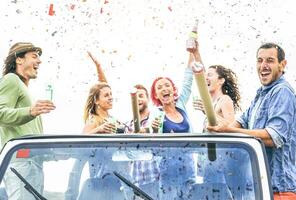 groep van gelukkig vrienden maken partij het werpen confetti Aan converteerbaar jeep auto - jong mensen vieren en hebben pret drinken Champagne en lachend samen buitenshuis - jeugd levensstijl concept foto