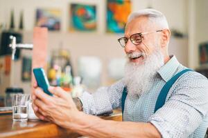 hipster Mens gebruik makend van mobiel telefoon terwijl zittend in een bar - senior mannetje aan het kijken Aan nieuw trends smartphone apps voor sociaal media - technologie en mensen levensstijl concept foto