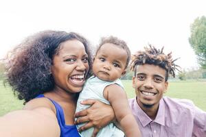 gelukkig Afrikaanse familie nemen een selfie met mobiel telefoon in een openbaar park buitenshuis - moeder en vader hebben pret met hun dochter gedurende een weekend zonnig dag - liefde en concept geluk foto